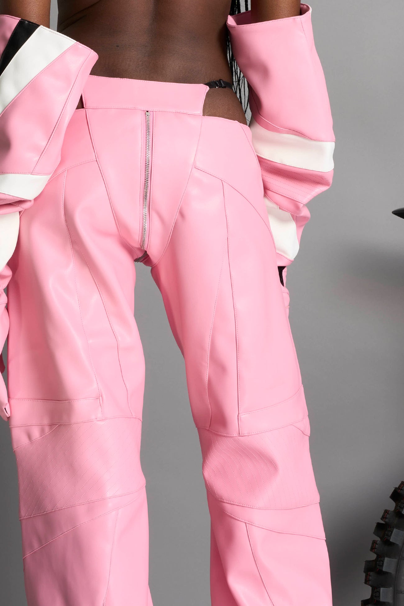 Low-rise flared pants in pink faux leather with bold side cut-outs and thong strap detailing. Featuring moto-style paneling, front zip closure, and a sculpted fit. A statement piece for rave, nightlife, and runway-inspired looks.