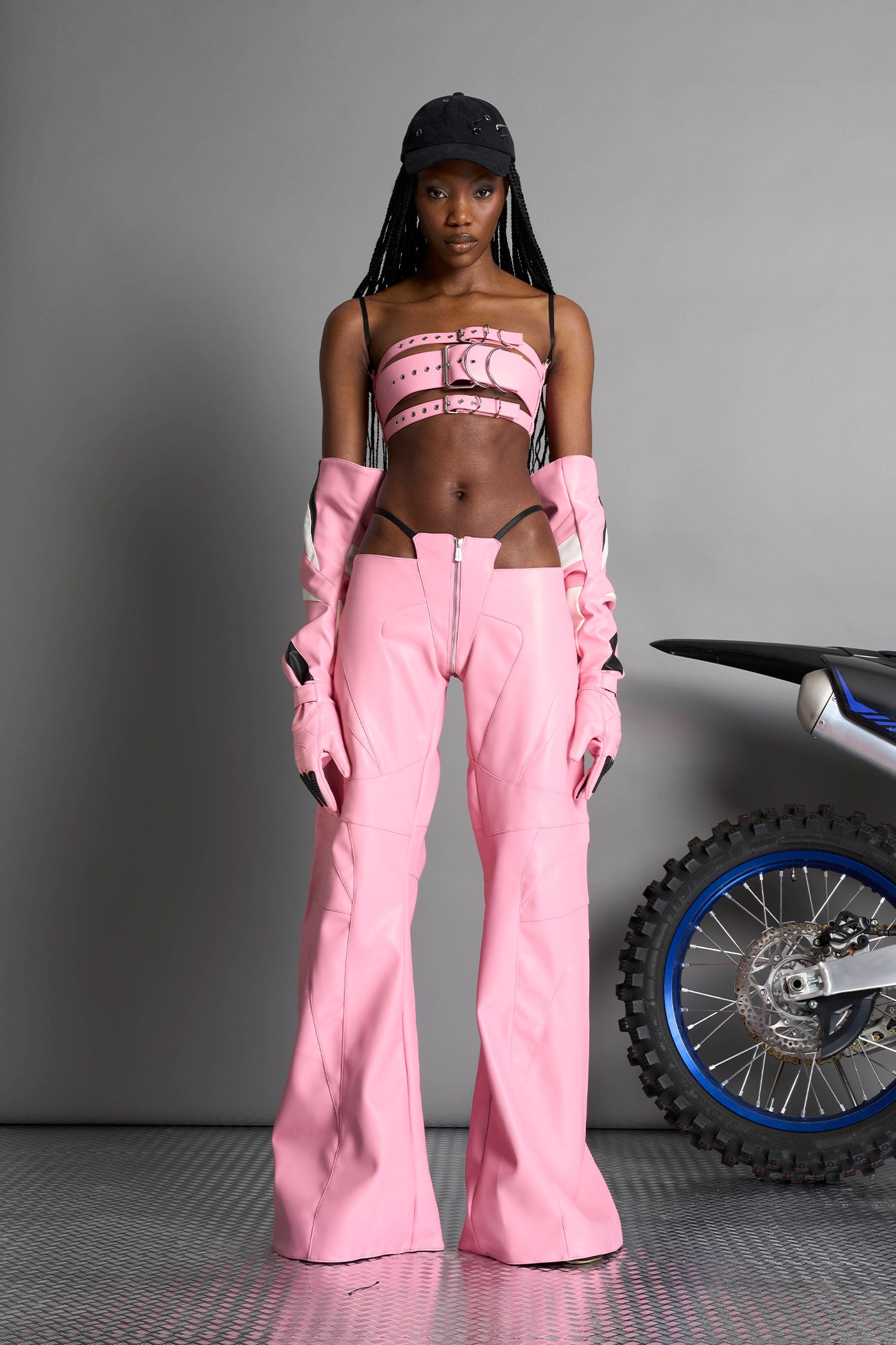 Low-rise flared pants in pink faux leather with bold side cut-outs and thong strap detailing. Featuring moto-style paneling, front zip closure, and a sculpted fit. A statement piece for rave, nightlife, and runway-inspired looks.