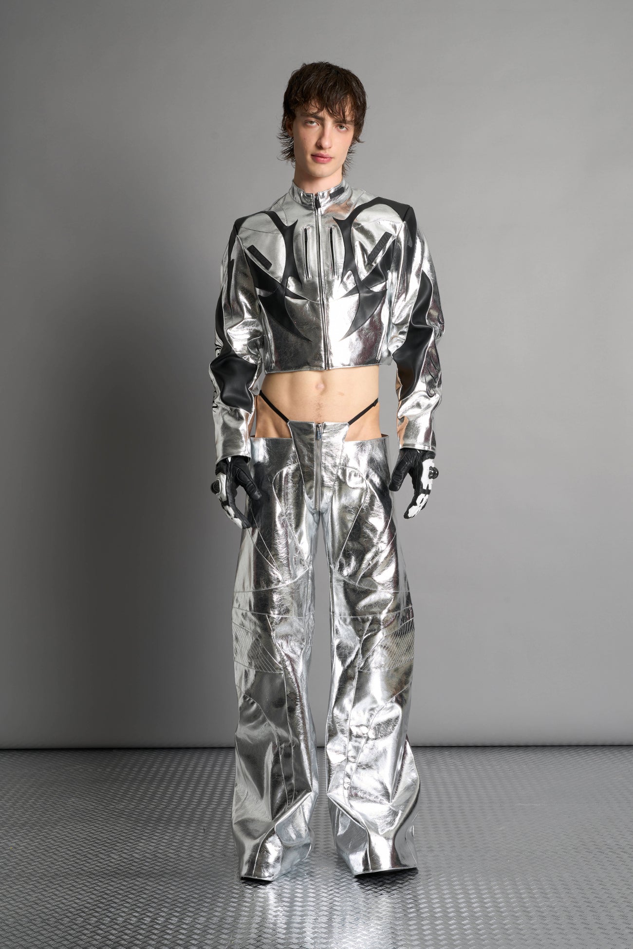 Low-rise flared pants in silver faux leather with bold side cut-outs and thong strap detailing. Featuring moto-style paneling, front zip closure, and a sculpted fit. A statement piece for rave, nightlife, and runway-inspired looks.