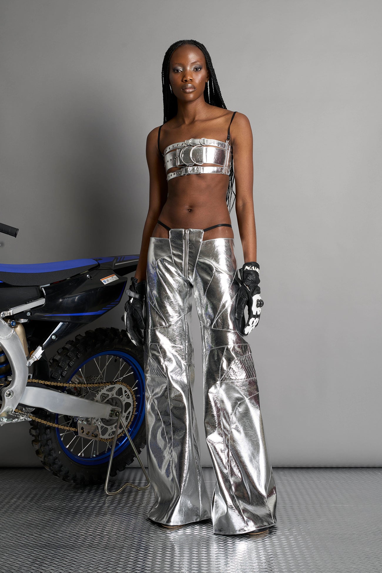 Low-rise flared pants in silver faux leather with bold side cut-outs and thong strap detailing. Featuring moto-style paneling, front zip closure, and a sculpted fit. A statement piece for rave, nightlife, and runway-inspired looks.