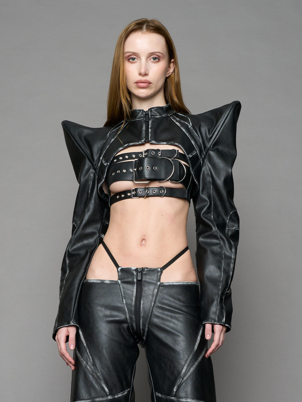 Model wearing a black vegan leather spike shoulder bolero jacket with cut-out design on a gray background
