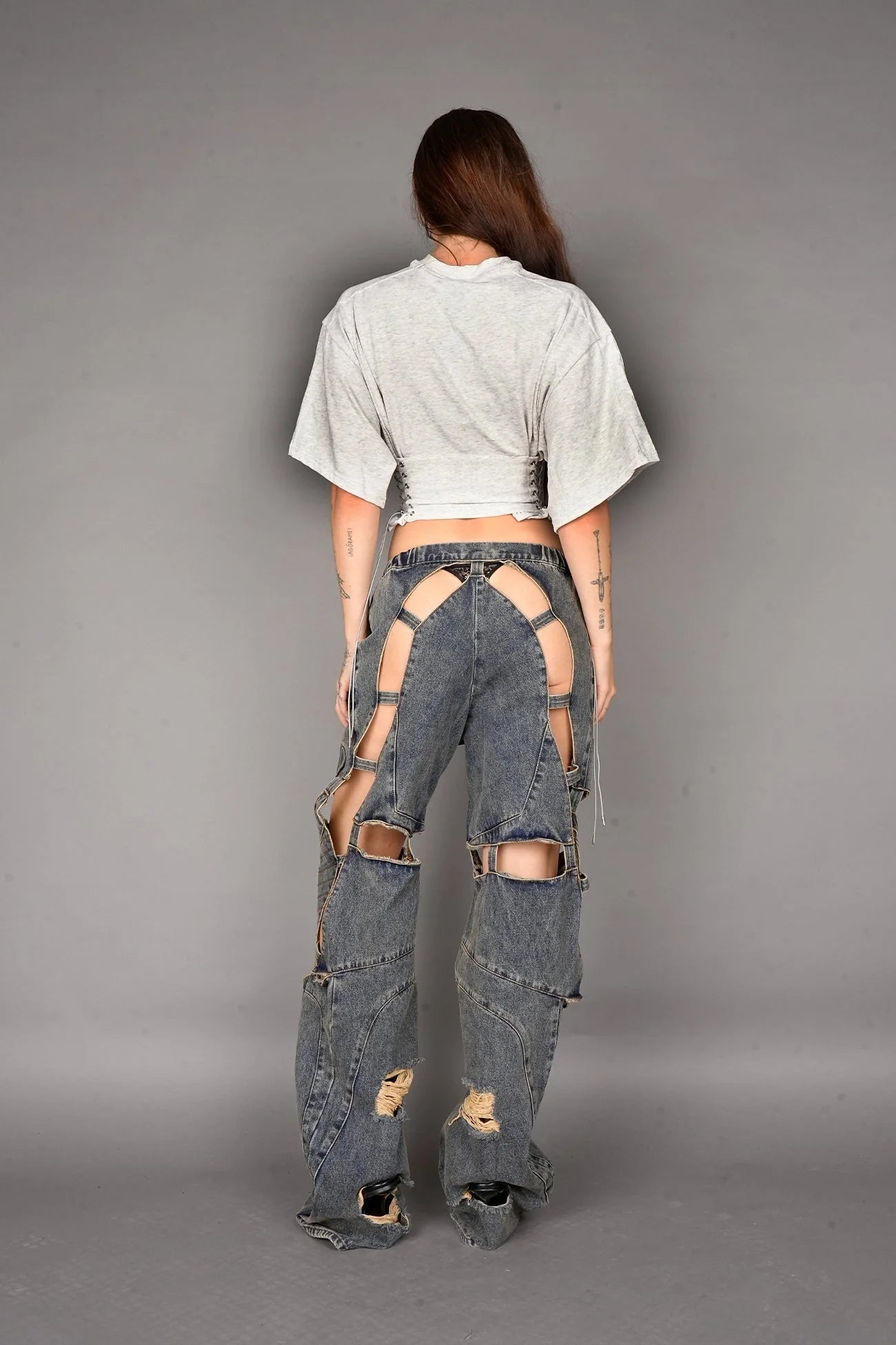 Person wearing a grey crop top and ripped jeans on a gray background