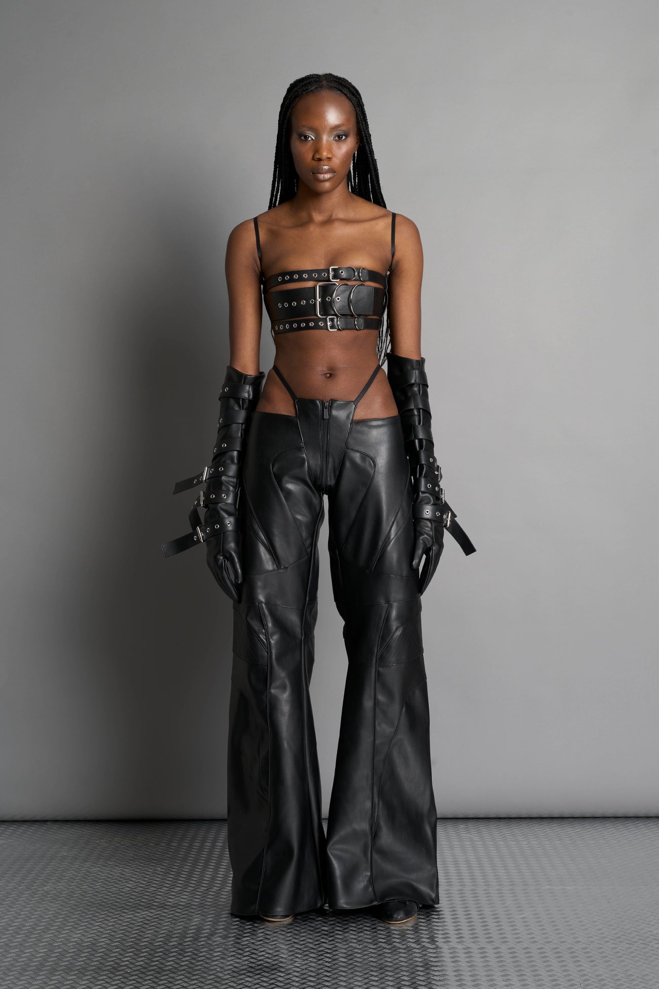 Black vegan leather belt top with three adjustable grommet straps, oversized metal buckles, and circular hardware – edgy bondage-inspired crop top for festival or clubwear.