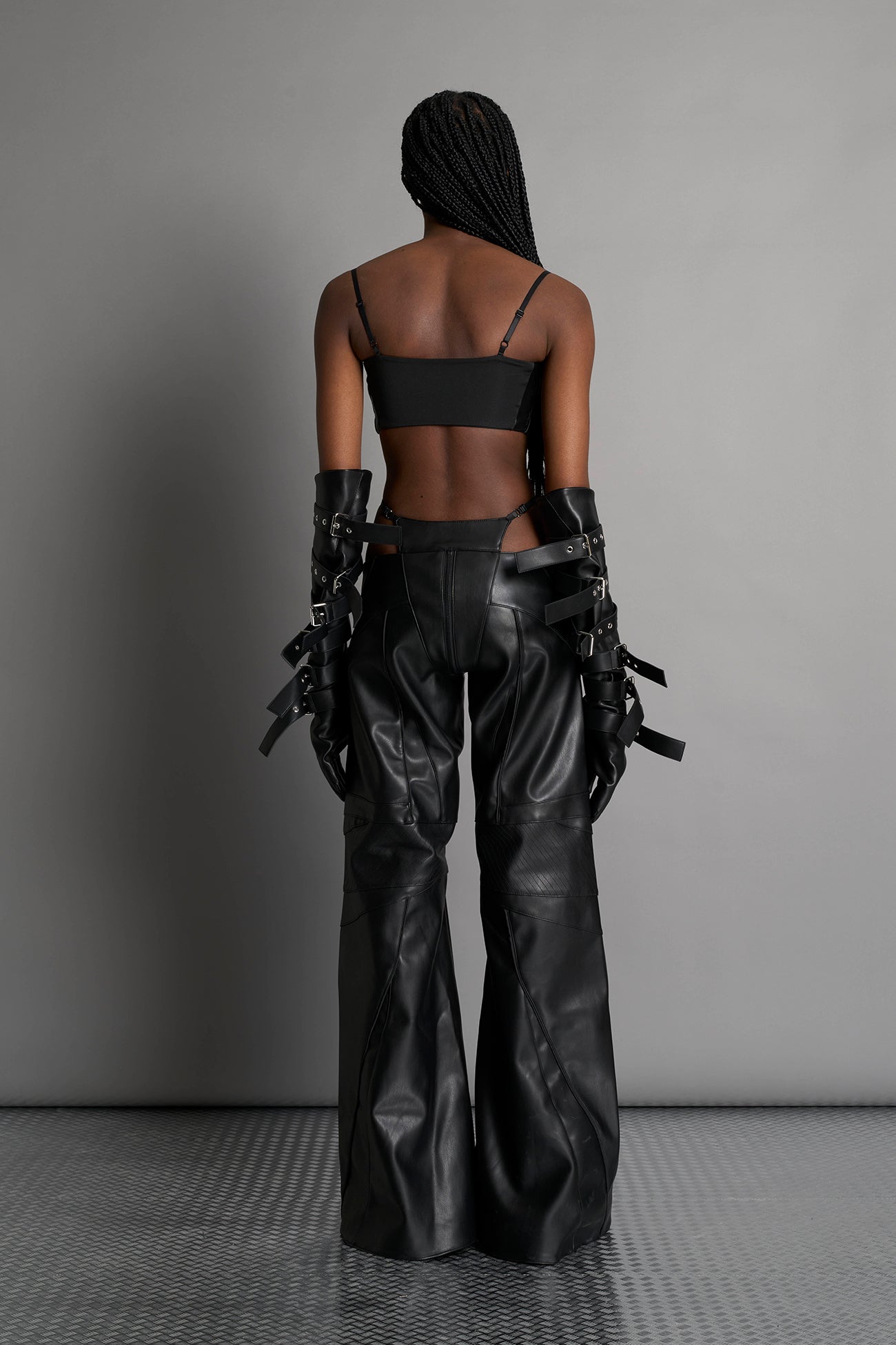 Low-rise flared pants in black faux leather with bold side cut-outs and thong strap detailing. Featuring moto-style paneling, front zip closure, and a sculpted fit. A statement piece for rave, nightlife, and runway-inspired looks.