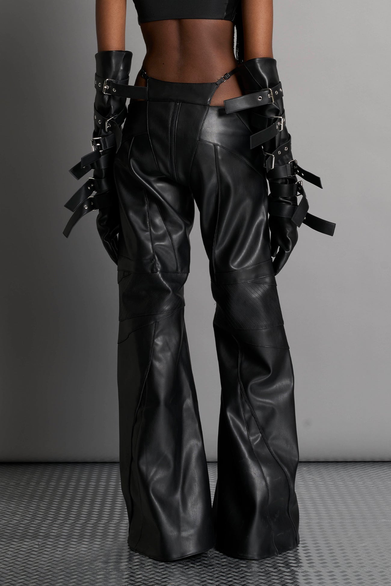 Low-rise flared pants in black faux leather with bold side cut-outs and thong strap detailing. Featuring moto-style paneling, front zip closure, and a sculpted fit. A statement piece for rave, nightlife, and runway-inspired looks.