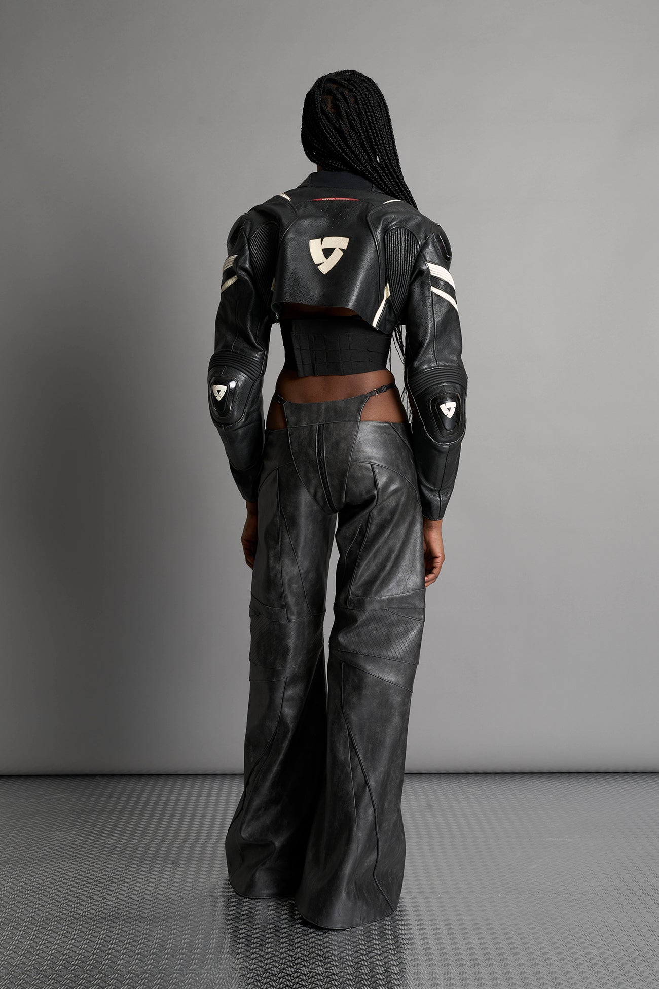 Low-rise flared pants in washed black faux leather with bold side cut-outs and thong strap detailing. Featuring moto-style paneling, front zip closure, and a sculpted fit. A statement piece for rave, nightlife, and runway-inspired looks.