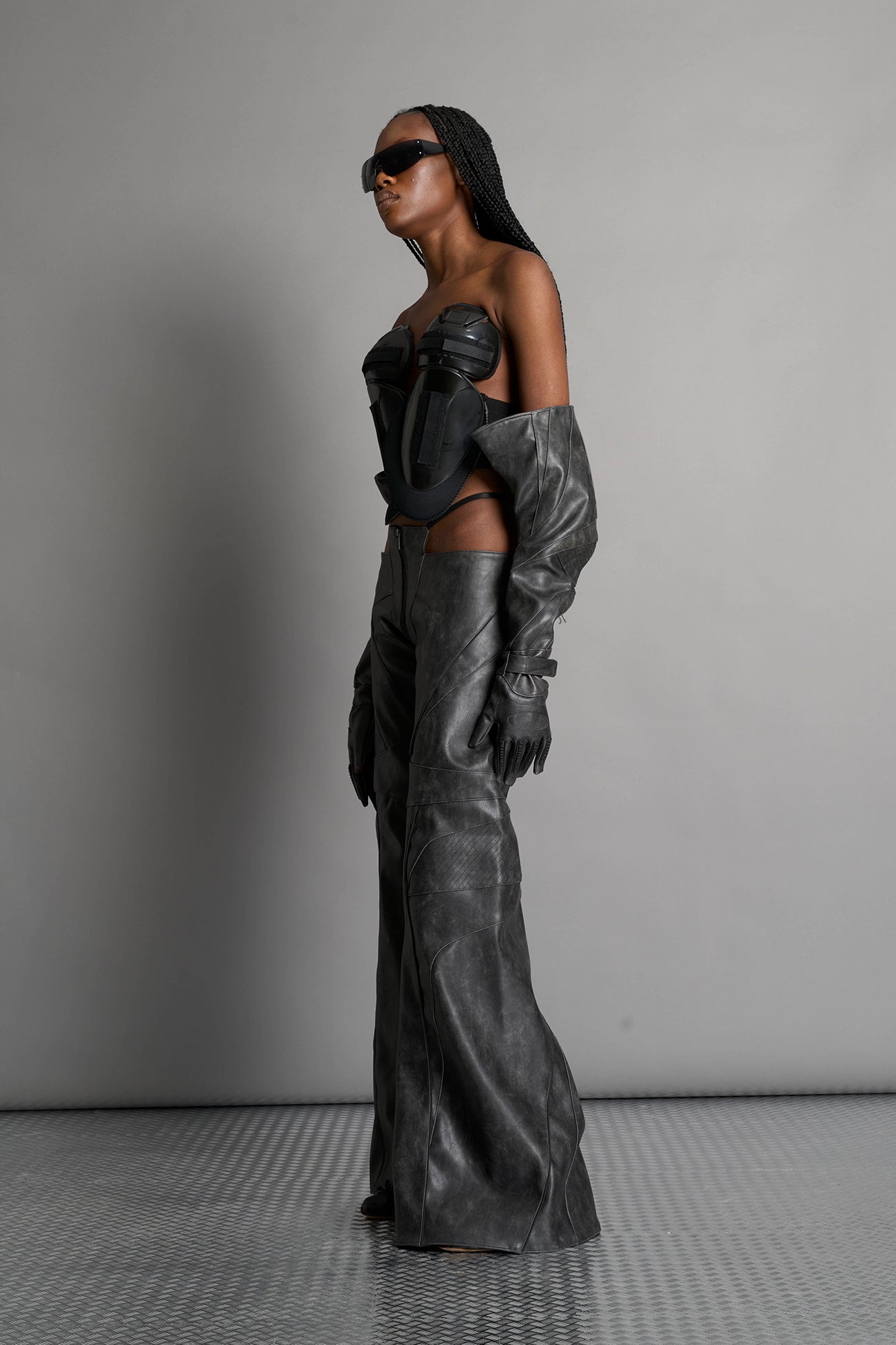 Low-rise flared pants in washed black faux leather with bold side cut-outs and thong strap detailing. Featuring moto-style paneling, front zip closure, and a sculpted fit. A statement piece for rave, nightlife, and runway-inspired looks.