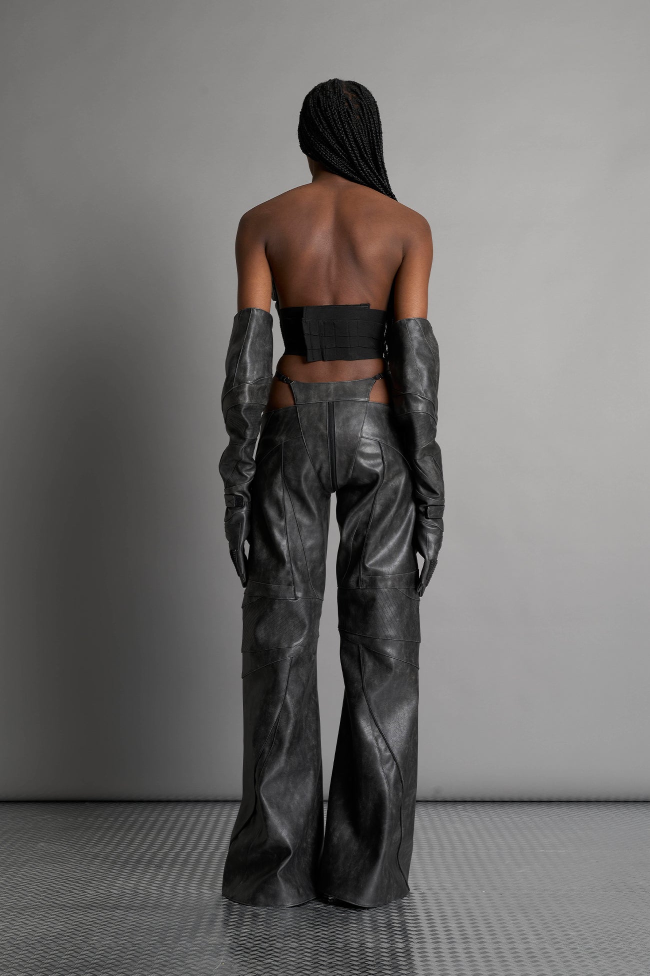 Low-rise flared pants in washed black faux leather with bold side cut-outs and thong strap detailing. Featuring moto-style paneling, front zip closure, and a sculpted fit. A statement piece for rave, nightlife, and runway-inspired looks.