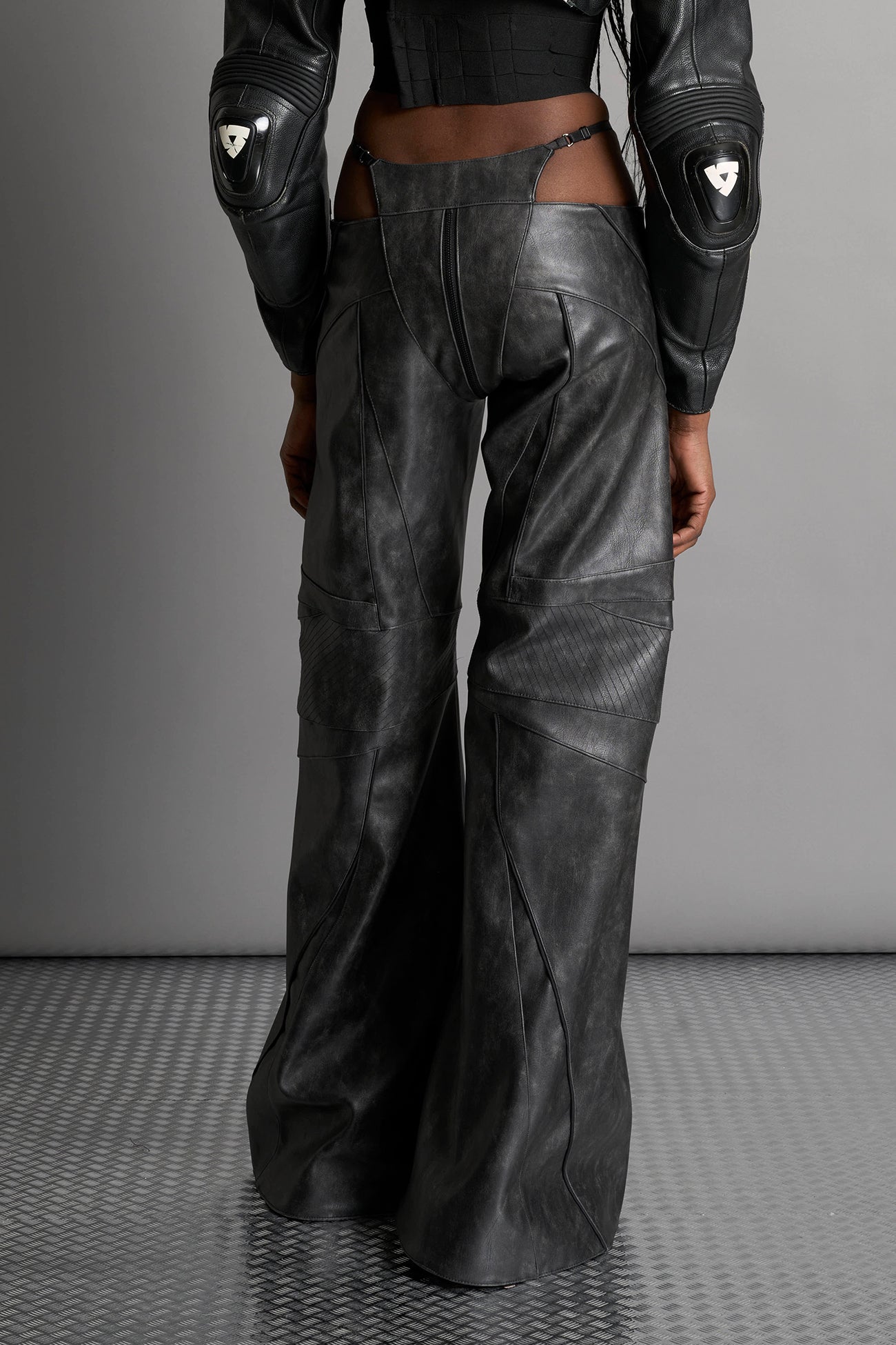 Low-rise flared pants in washed black faux leather with bold side cut-outs and thong strap detailing. Featuring moto-style paneling, front zip closure, and a sculpted fit. A statement piece for rave, nightlife, and runway-inspired looks.