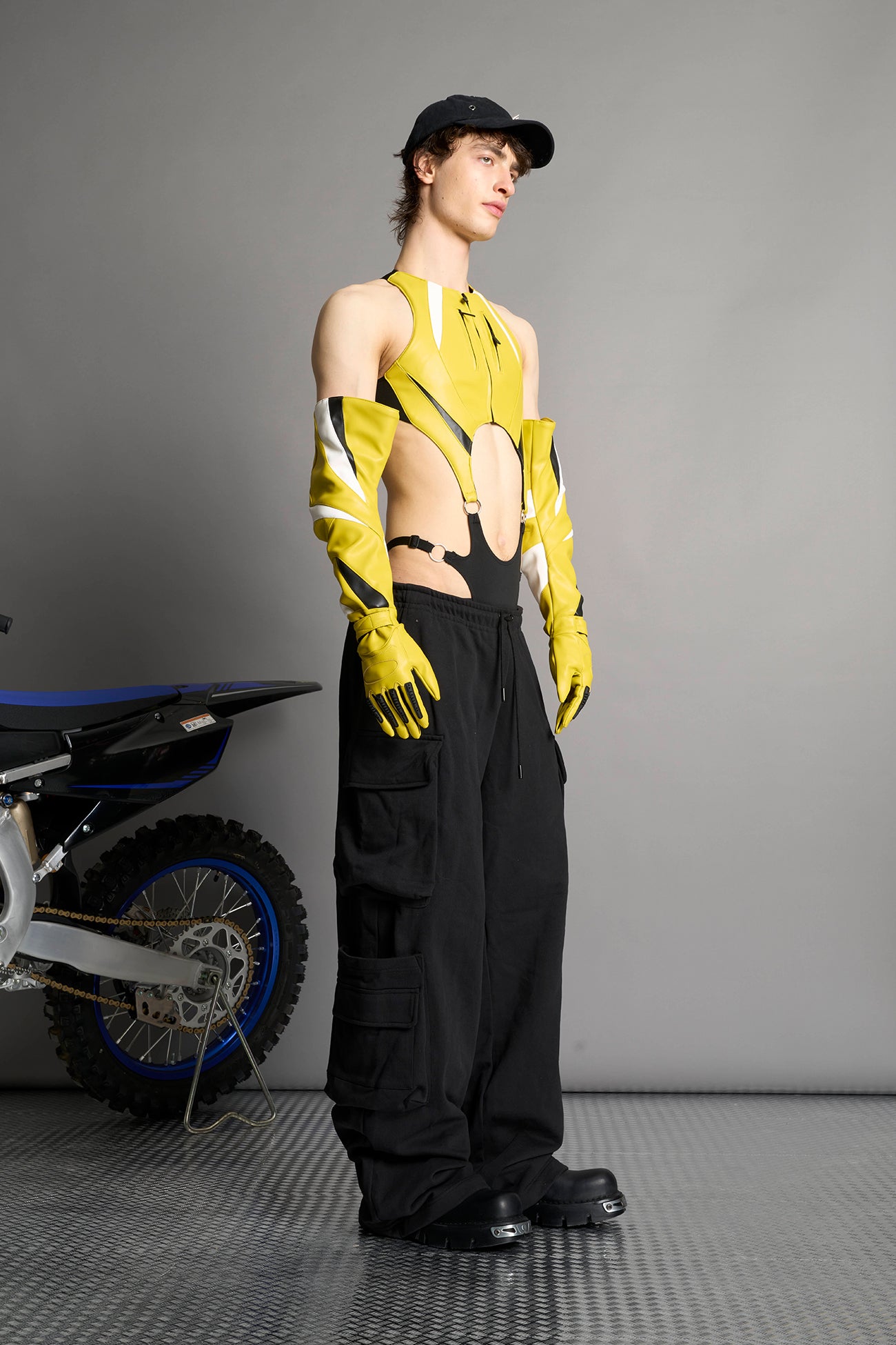 model wears yellow vegan leather elbow-length moto gloves with motocross-style lines, contrast panelling, rubber finger protection, lycra webbing, and velcro wrist fasteners.