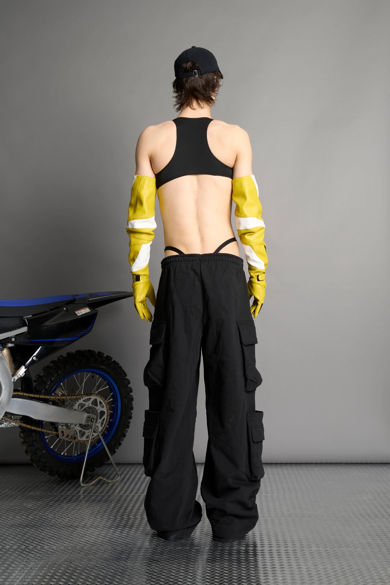 model wears yellow vegan leather elbow-length moto gloves with motocross-style lines, contrast panelling, rubber finger protection, lycra webbing, and velcro wrist fasteners.