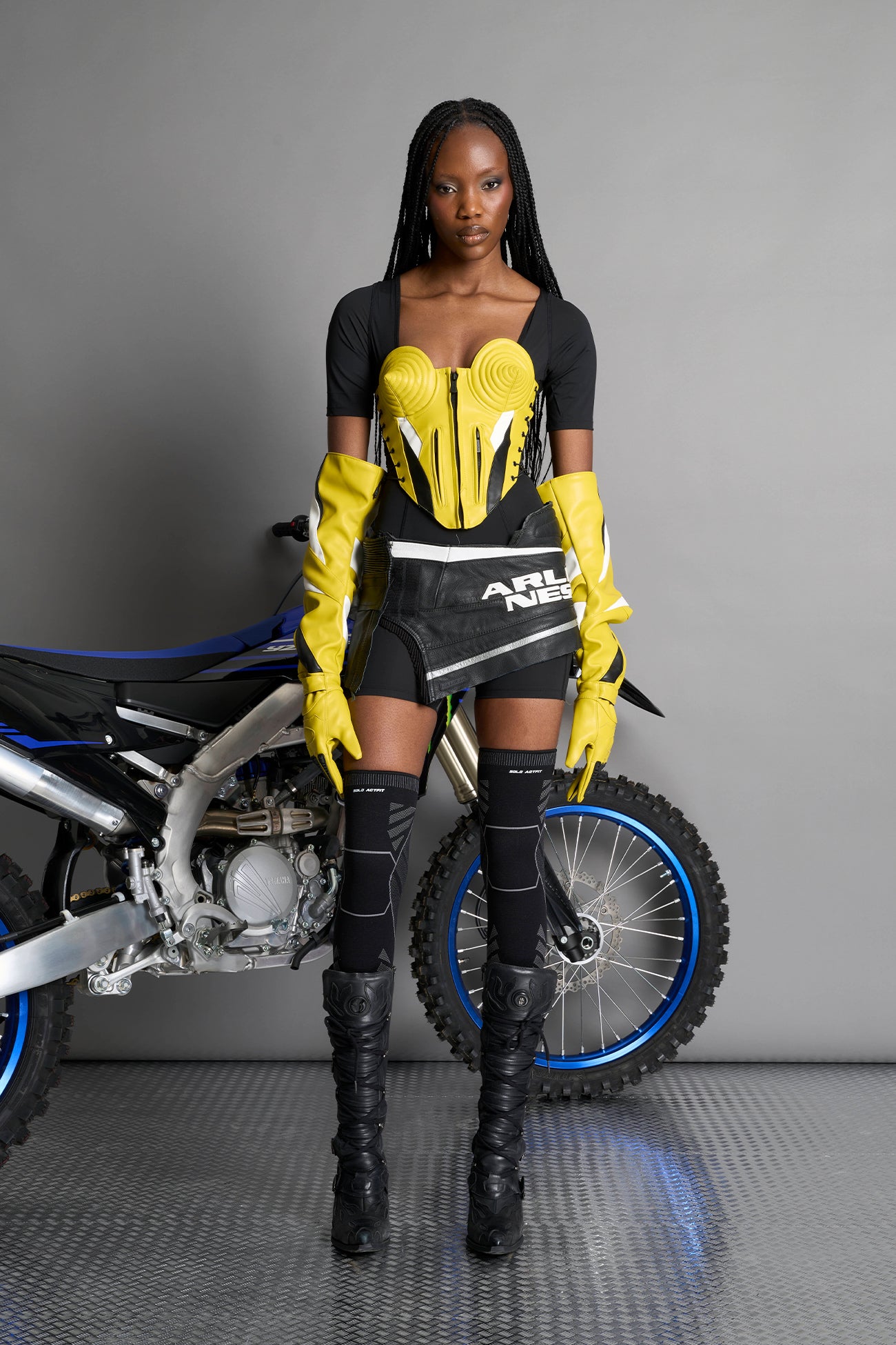 model wears yellow vegan leather elbow-length moto gloves with motocross-style lines, contrast panelling, rubber finger protection, lycra webbing, and velcro wrist fasteners.
