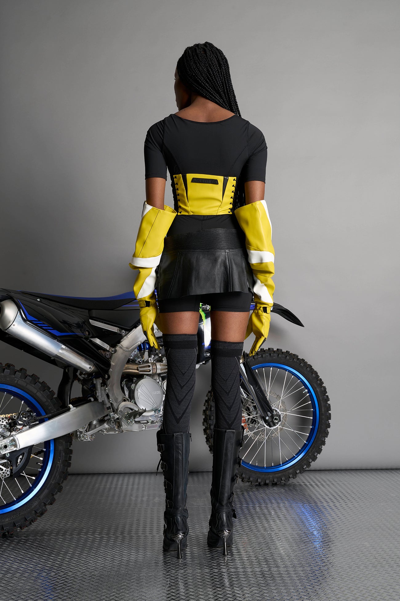 model wears yellow vegan leather elbow-length moto gloves with motocross-style lines, contrast panelling, rubber finger protection, lycra webbing, and velcro wrist fasteners.