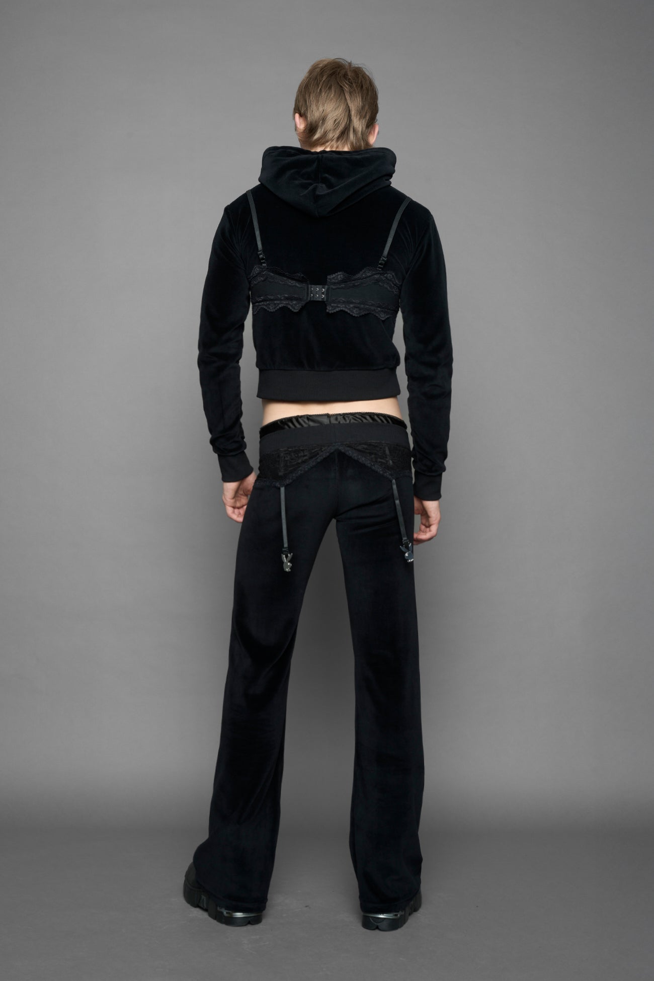 A female model wearing black velvet tracksuit pants with a lingerie black lace garter and suspenders with metal silver Bunnys
