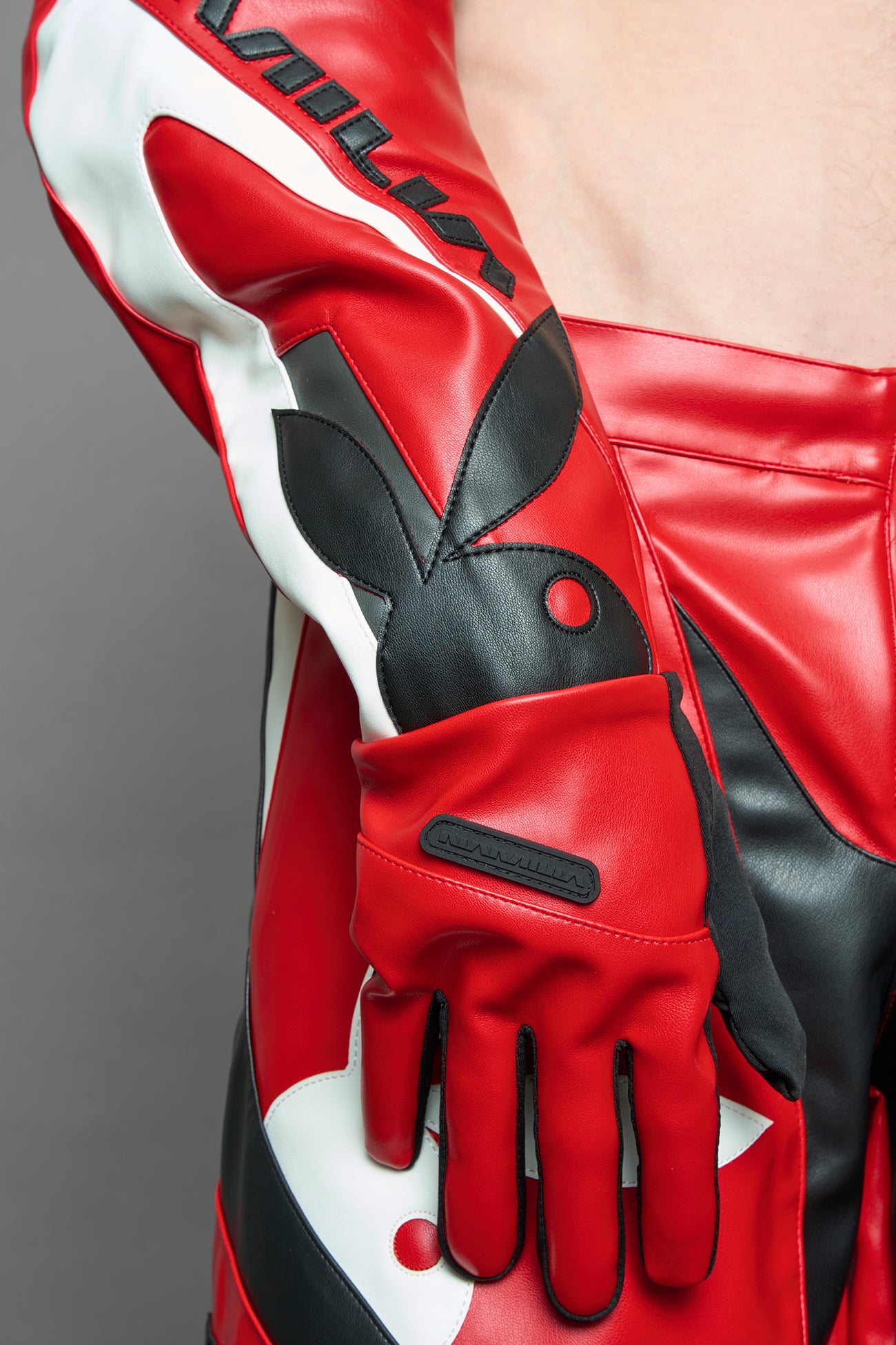 A model wears long motocross inspired red vegan Leather gloves with white and grey style paneling and black PU Leather 'Namilia' and 'Playboy' embroidery and a 'Playboy x Namilia' Rubbertag.