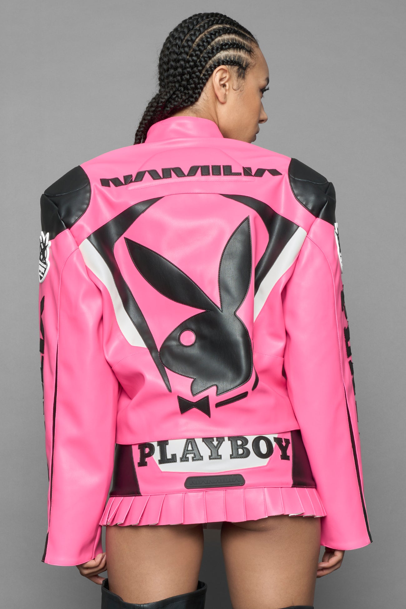 model wearing pink vegan leather zip-up jacket with black PU leather 'Namilia' and 'Playboy' embroidery and black and white paneling. On the left chest there is a white Playboy Bunny Embroidery.