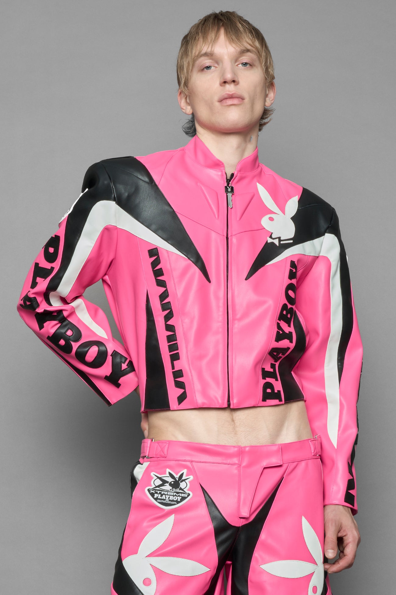 model wearing pink vegan leather zip-up jacket with black PU leather 'Namilia' and 'Playboy' embroidery and black and white paneling. On the left chest there is a white Playboy Bunny Embroidery.
