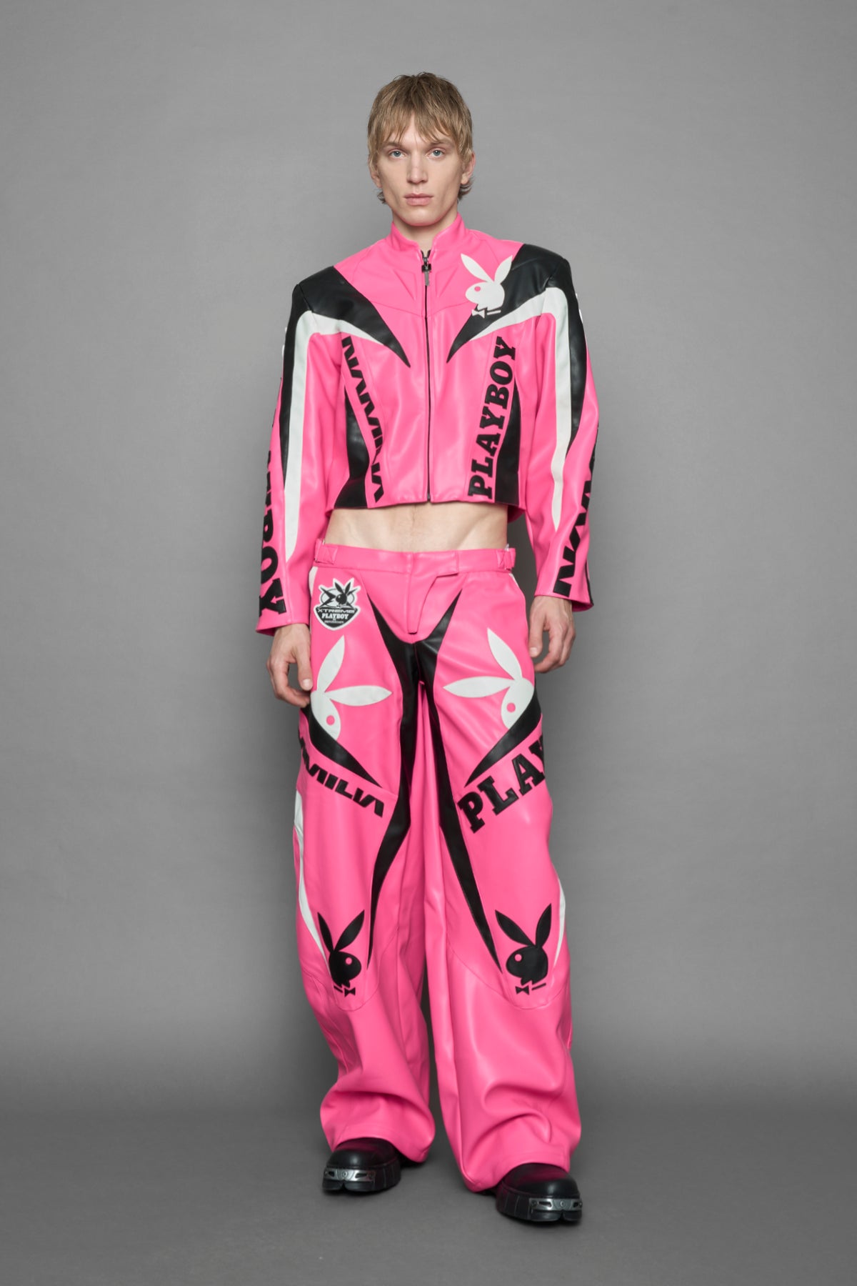 model wearing pink vegan leather zip-up jacket with black PU leather 'Namilia' and 'Playboy' embroidery and black and white paneling. On the left chest there is a white Playboy Bunny Embroidery.