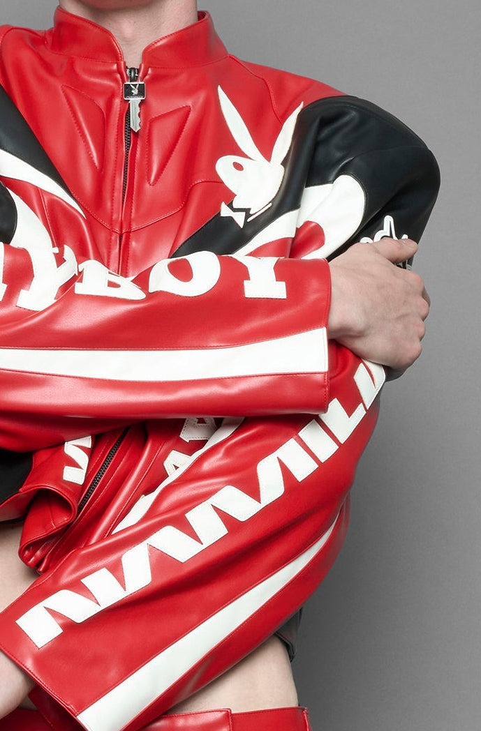 model wearing red vegan leather zip-up jacket with black PU leather 'Namilia' and 'Playboy' embroidery and black and white paneling. On the left chest there is a white Playboy Bunny Embroidery.