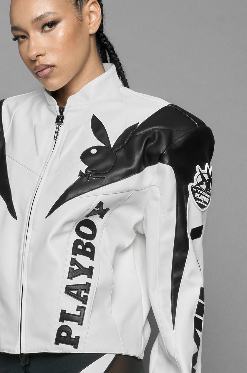 model wearing white vegan leather zip-up jacket with black PU leather 'Namilia' and 'Playboy' embroidery and black and white paneling. On the left chest there is a white Playboy Bunny Embroidery.