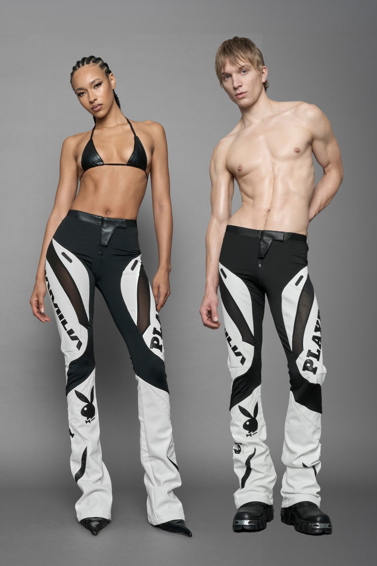 model wearing a white and black form fitted Pants with PU Leather Embroidery of 'Namilia', 'Playboy'. The pants have black Mesh fabric panels and are slightly flared from knee to hem