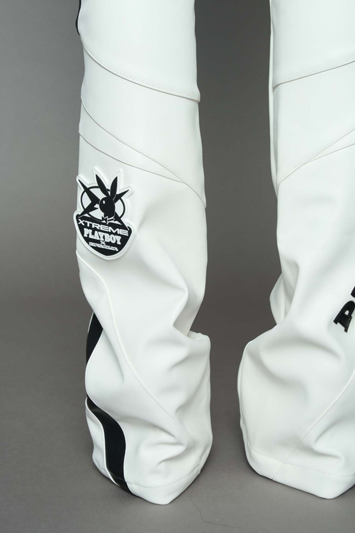 A female model wearing a white and black form fitted Pants with PU Leather Embroidery of 'Namilia', 'Playboy'. The pants have black Mesh fabric panels and are slightly flared from knee to hem