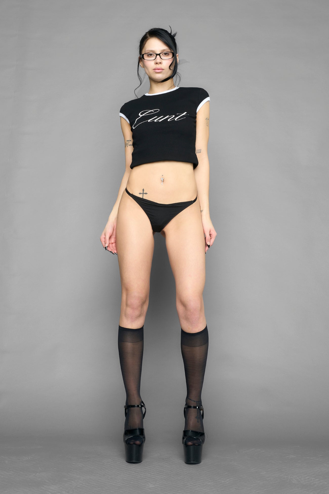 Model wearing black metal logo thong with adjustable straps, styled with cropped tee and heels, side view