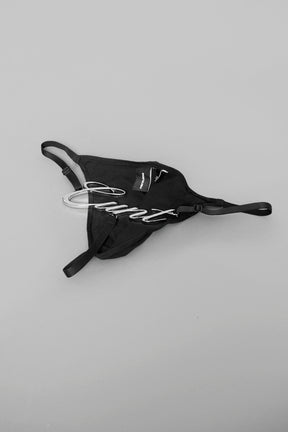 Model wearing black metal logo thong with adjustable straps