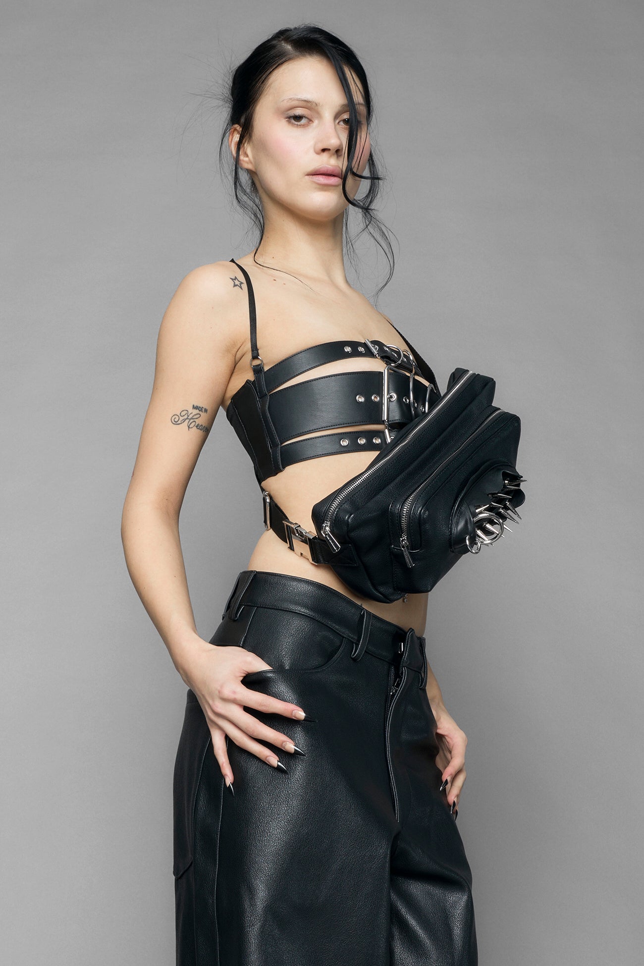 black vulva bum bag with adjustable strap and metal spike detailing worn as crossbody and shoulder bag studio ecommerce image