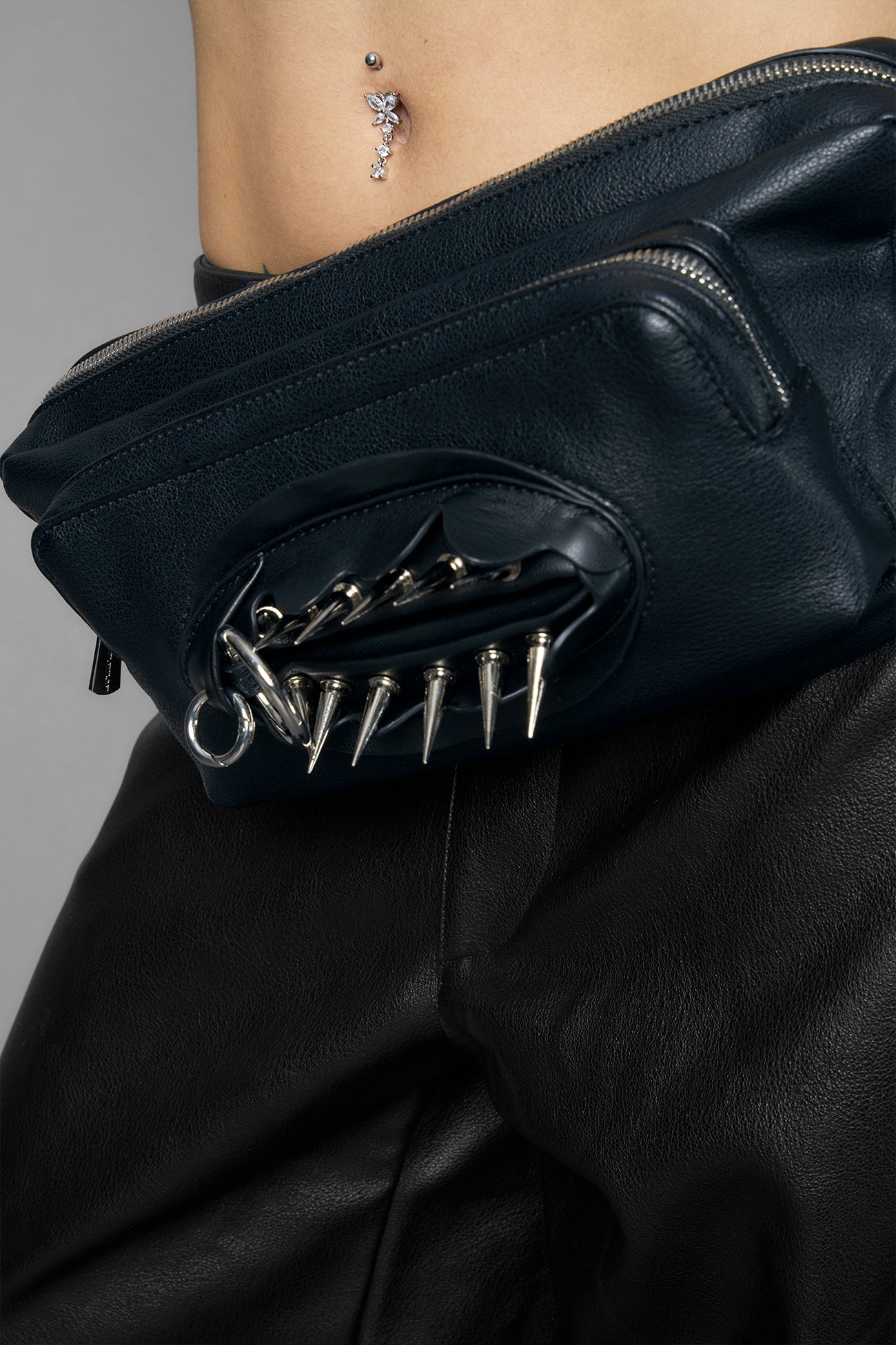 black vulva bum bag with adjustable strap and metal spike detailing worn as crossbody and shoulder bag studio ecommerce image