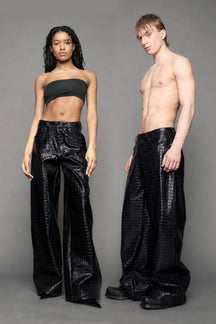 Two models wearing baggy suiting pants in black croc texture against a gray background