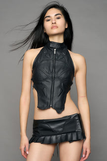 Black coated denim biker top by NAMILIA with high neck zip front, sculpted corset-style seams, open sides with string lacing, and criss-cross open back, worn by model on neutral background.