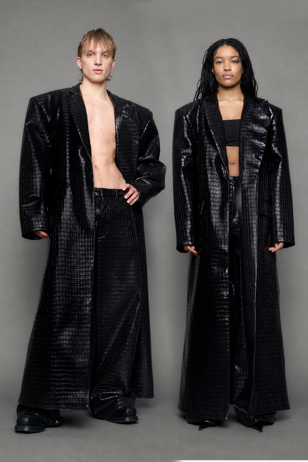 Two models wearing long black croc textured coat against a gray background