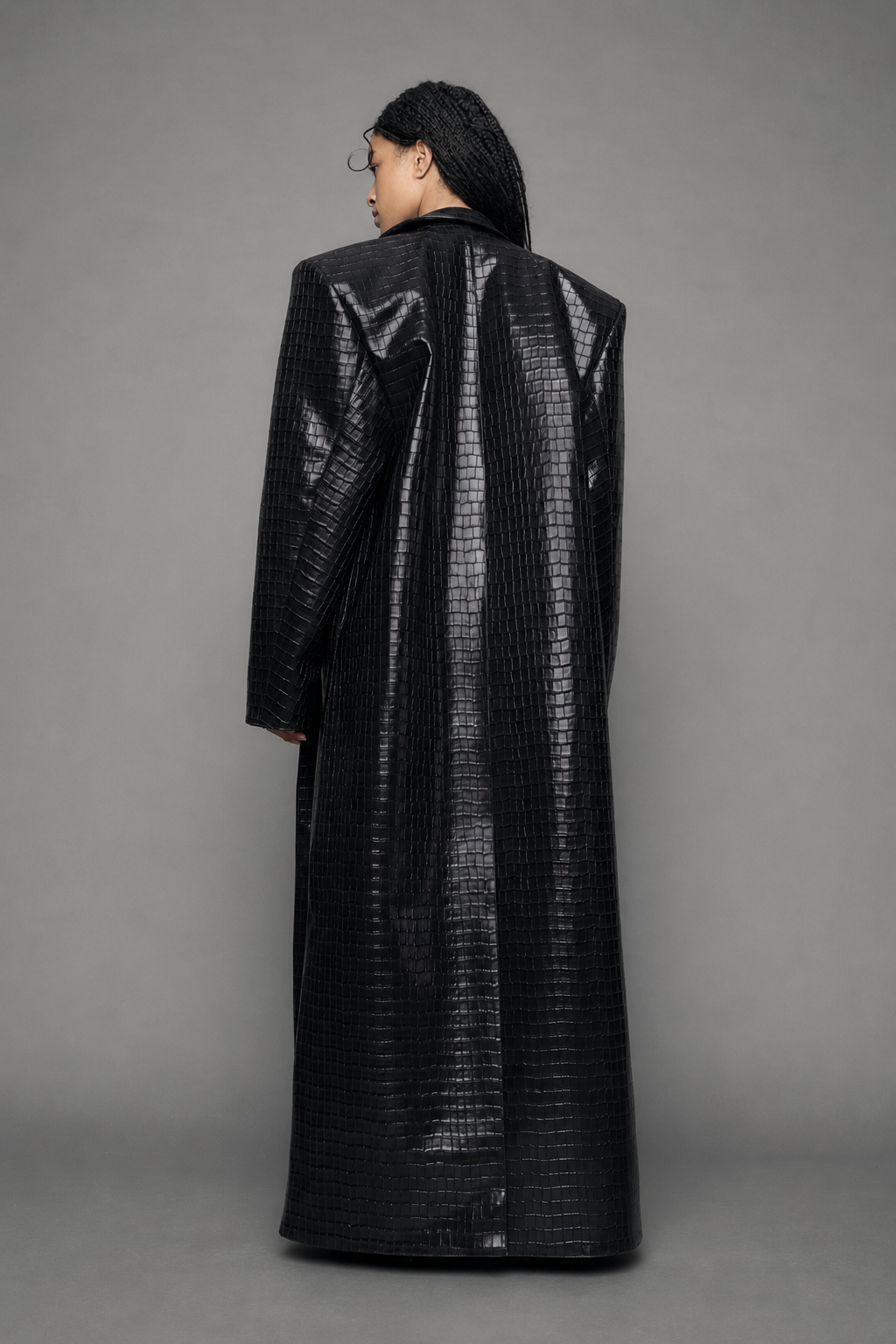 model wearing long black croc textured coat against a gray background