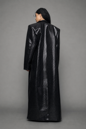 model wearing long black croc textured coat against a gray background
