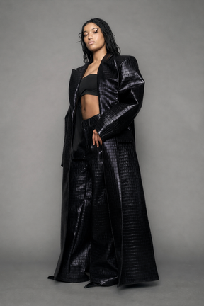 model wearing long black croc textured coat against a gray background