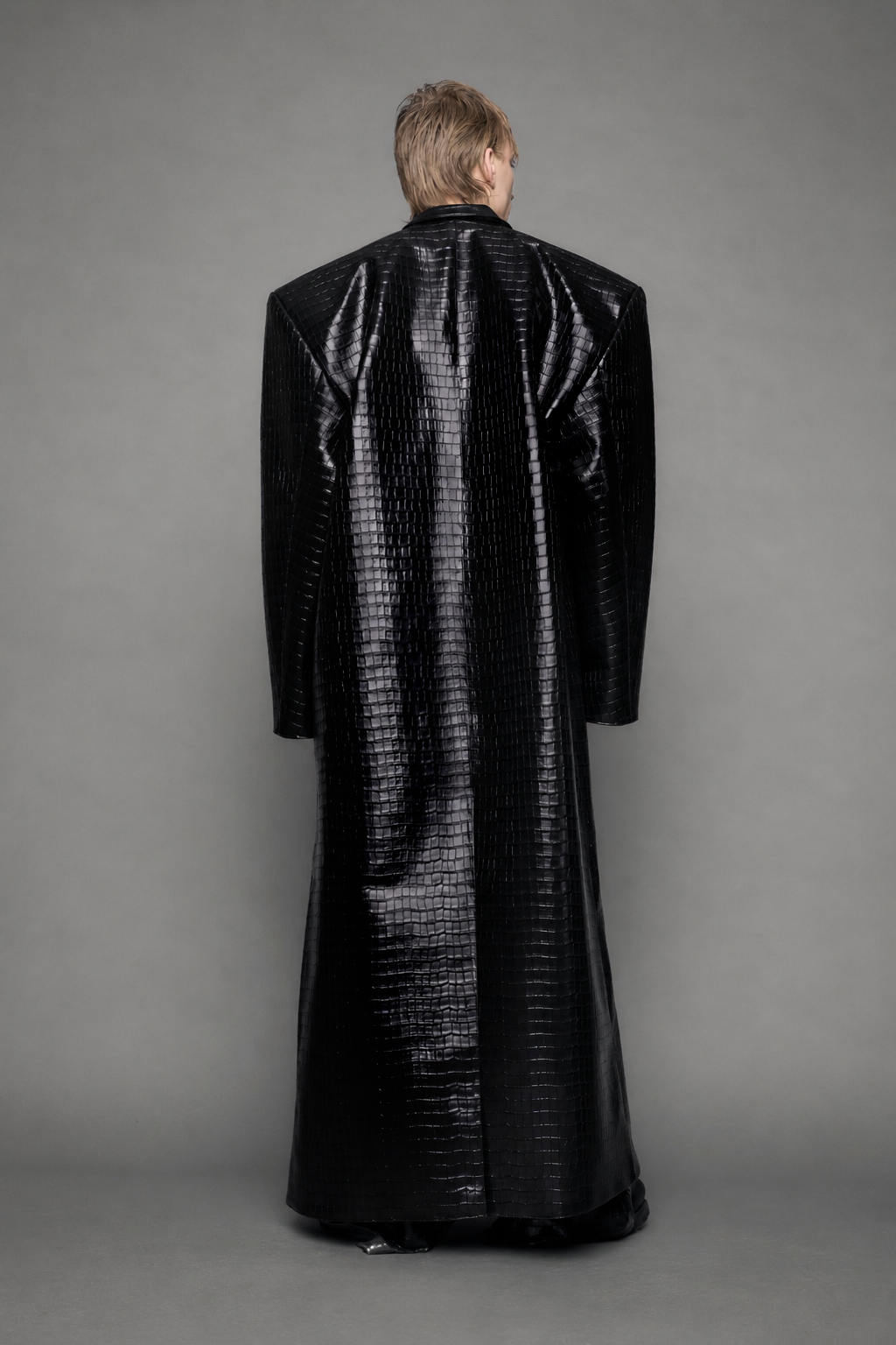 model wearing long black croc textured coat against a gray background