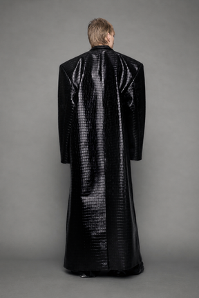 model wearing long black croc textured coat against a gray background