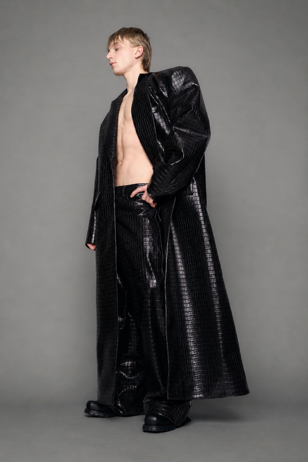 model wearing long black croc textured coat against a gray background