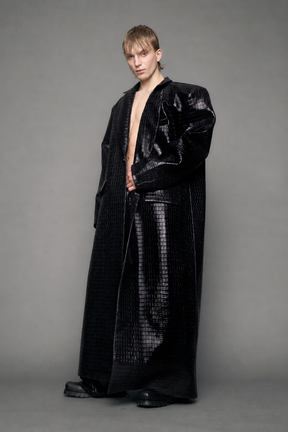 model wearing long black croc textured coat against a gray background