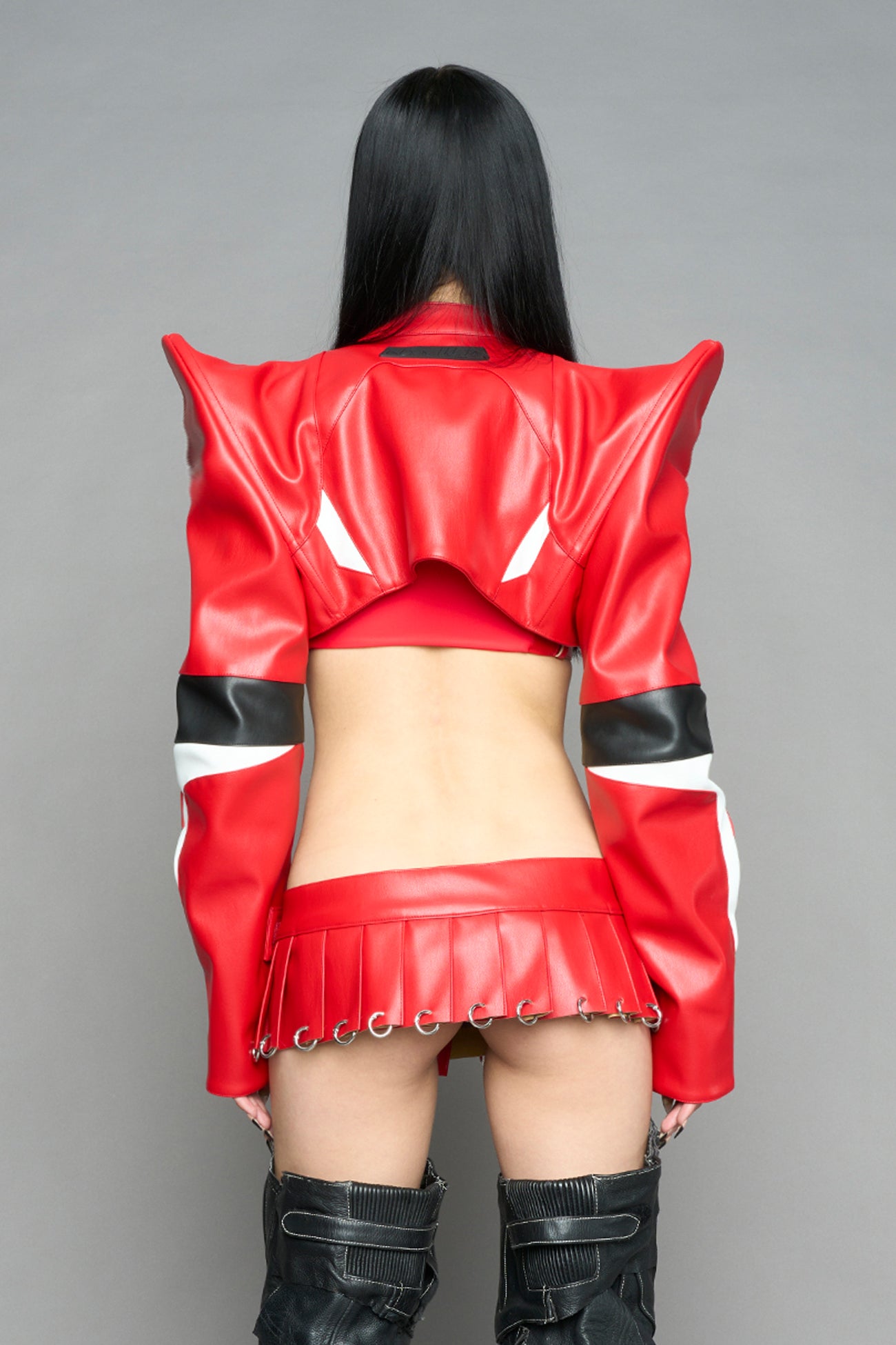 Model wears the red Namilia Spike Moto Bolero Jacket with wire shoulder pads, cropped hemline, branded front zipper, motocross-style lines, and black rubber logo tag on the back.