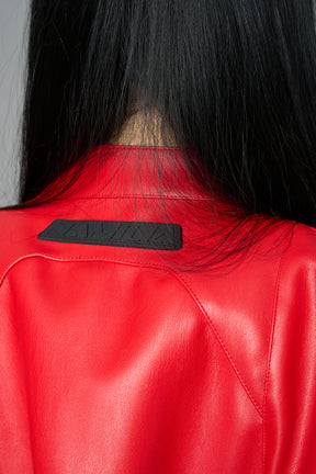 Model wears the red Namilia Spike Moto Bolero Jacket with wire shoulder pads, cropped hemline, branded front zipper, motocross-style lines, and black rubber logo tag on the back.