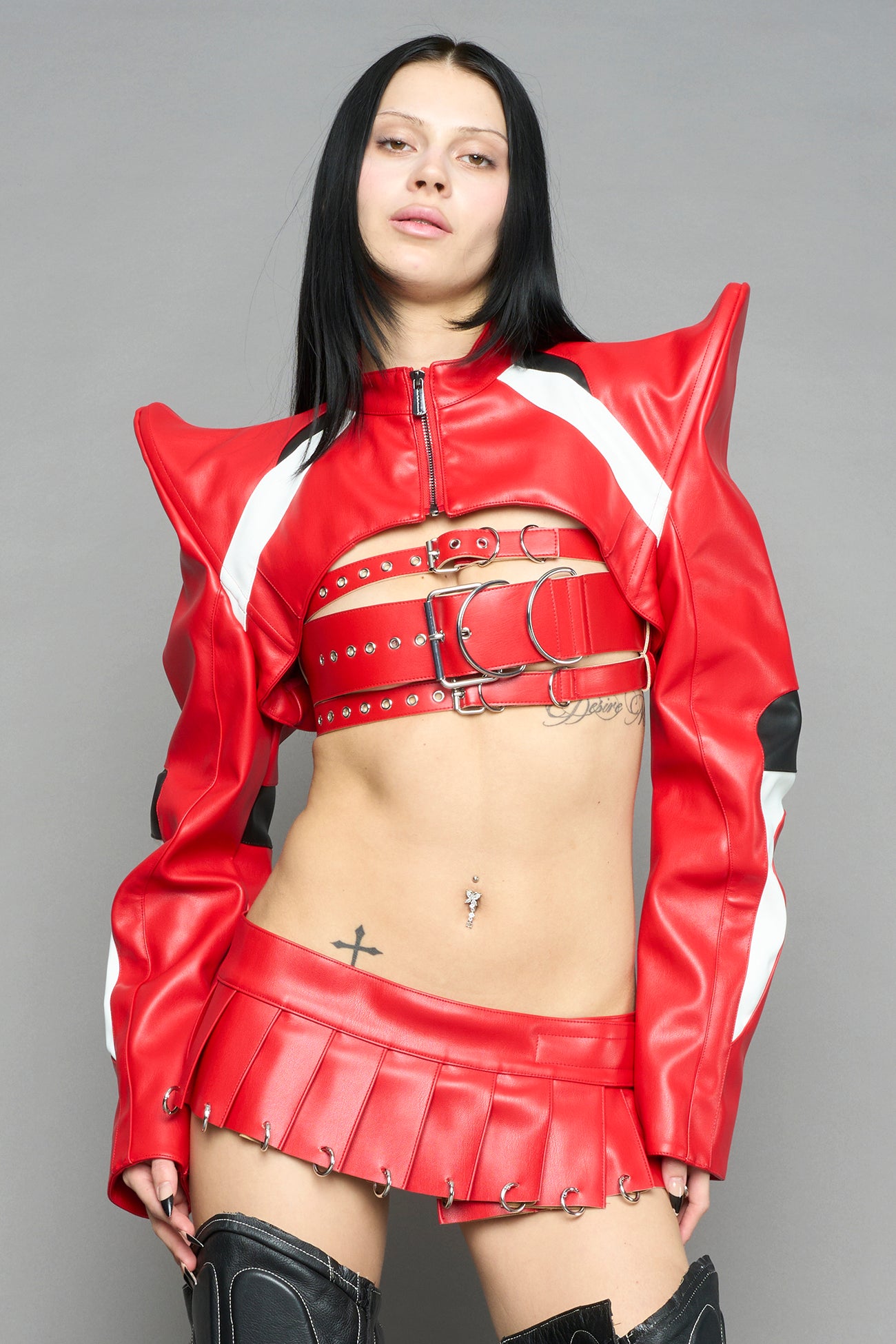 model wears the red Namilia Pleated Mini Skirt with ring piercing details on the hemline and velcro fold-over waistband closure.