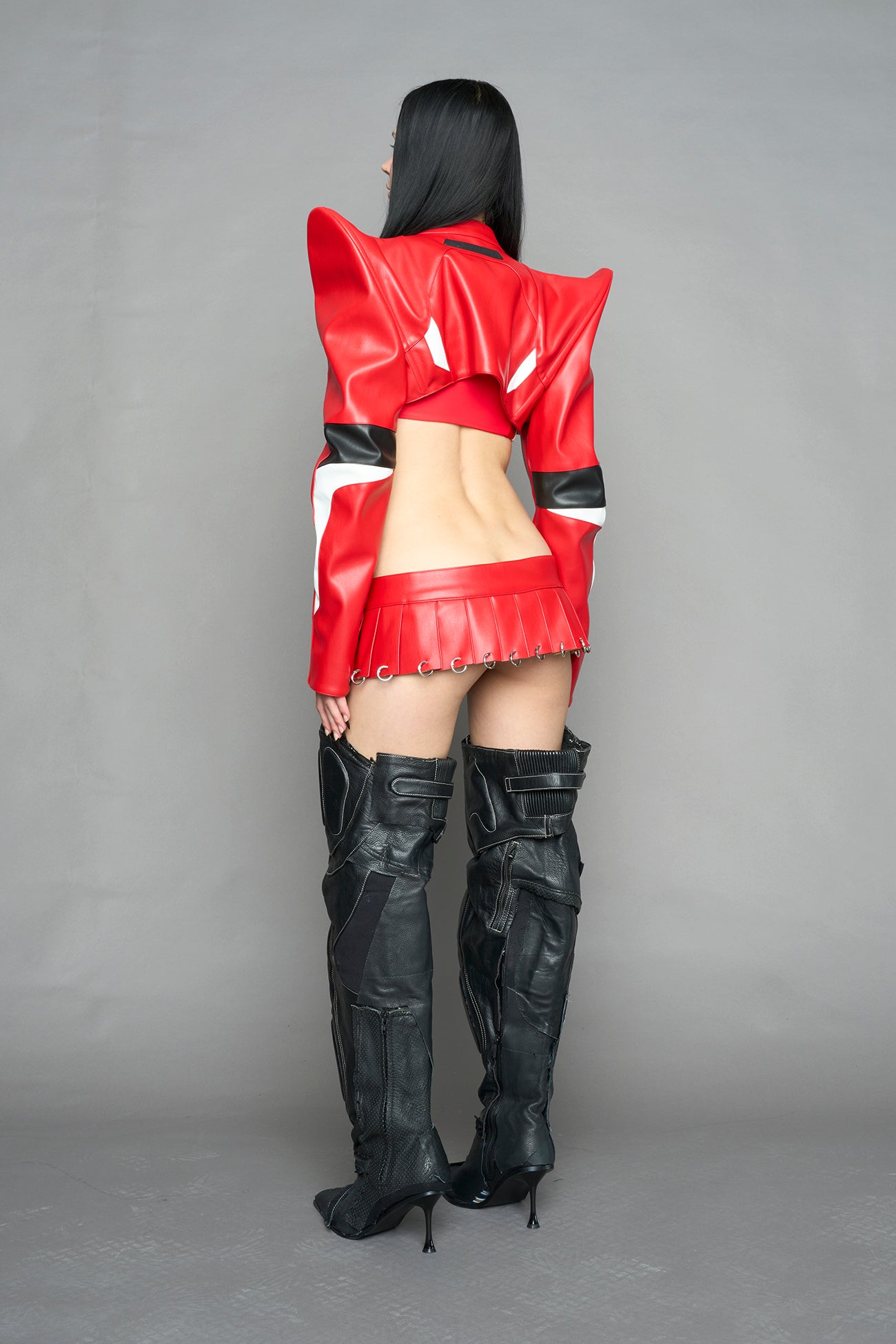 model wears the red Namilia Pleated Mini Skirt with ring piercing details on the hemline and velcro fold-over waistband closure.