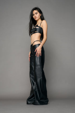 Low-rise flared pants in black faux leather with bold side cut-outs and thong strap detailing. Featuring moto-style paneling, front zip closure, and a sculpted fit. A statement piece for rave, nightlife, and runway-inspired looks.