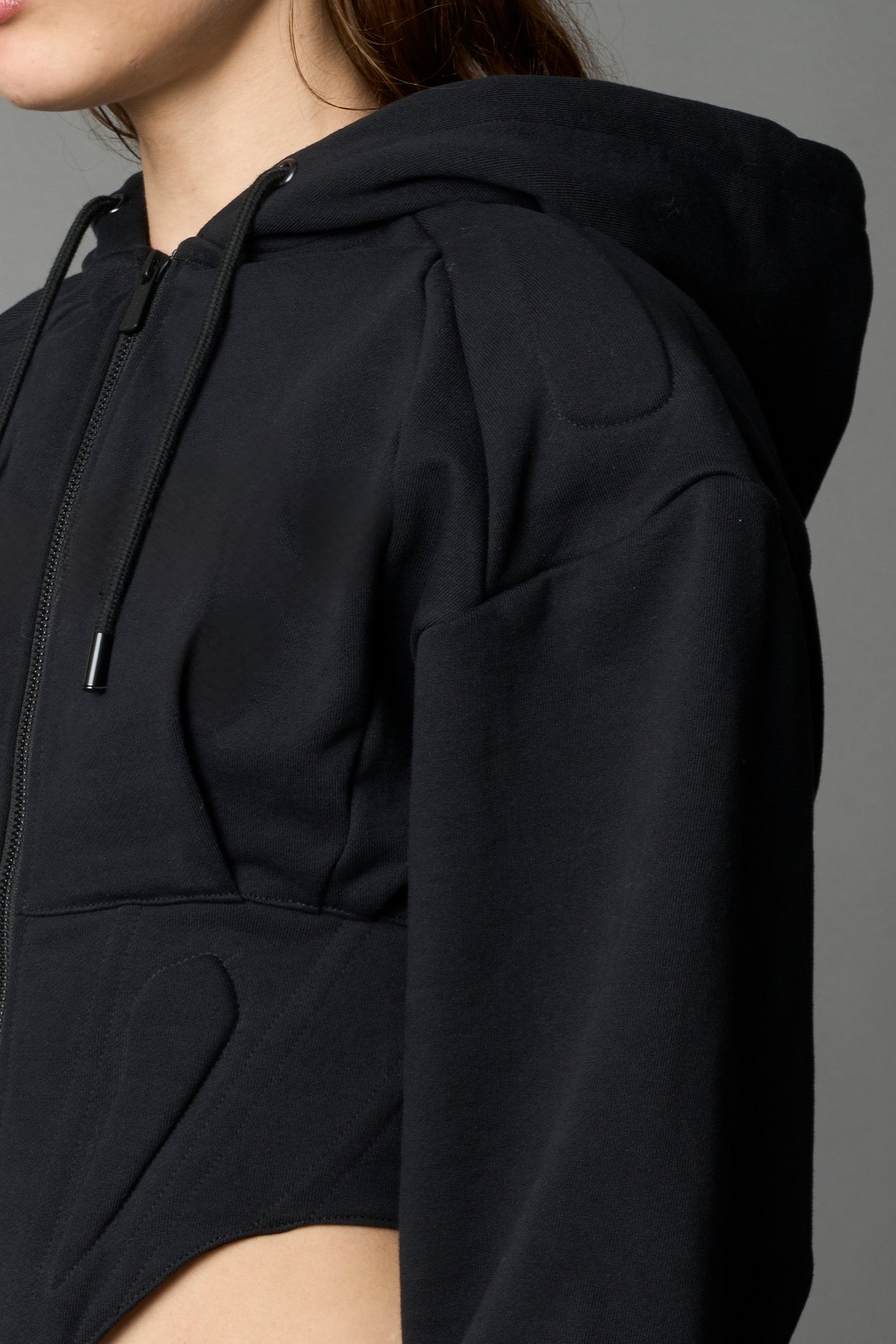 model in a black cropped hoodie featuring structured corset-style paneling  embroidered across the chest in tonal black