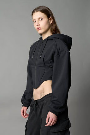 model in a black cropped hoodie featuring structured corset-style paneling  embroidered across the chest in tonal black