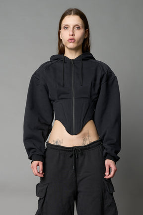 model in a black cropped hoodie featuring structured corset-style paneling  embroidered across the chest in tonal black