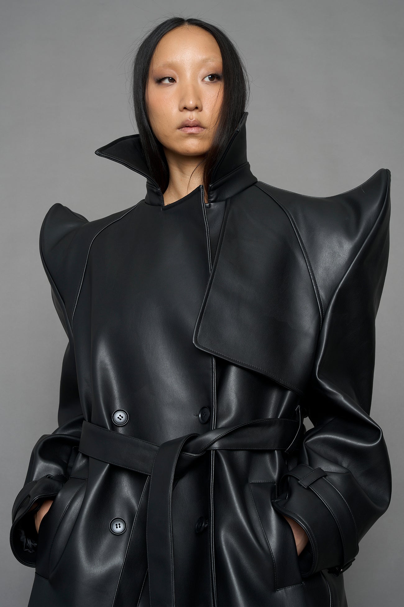 model wearing black vegan leather trench coat with sharp shoulder design
