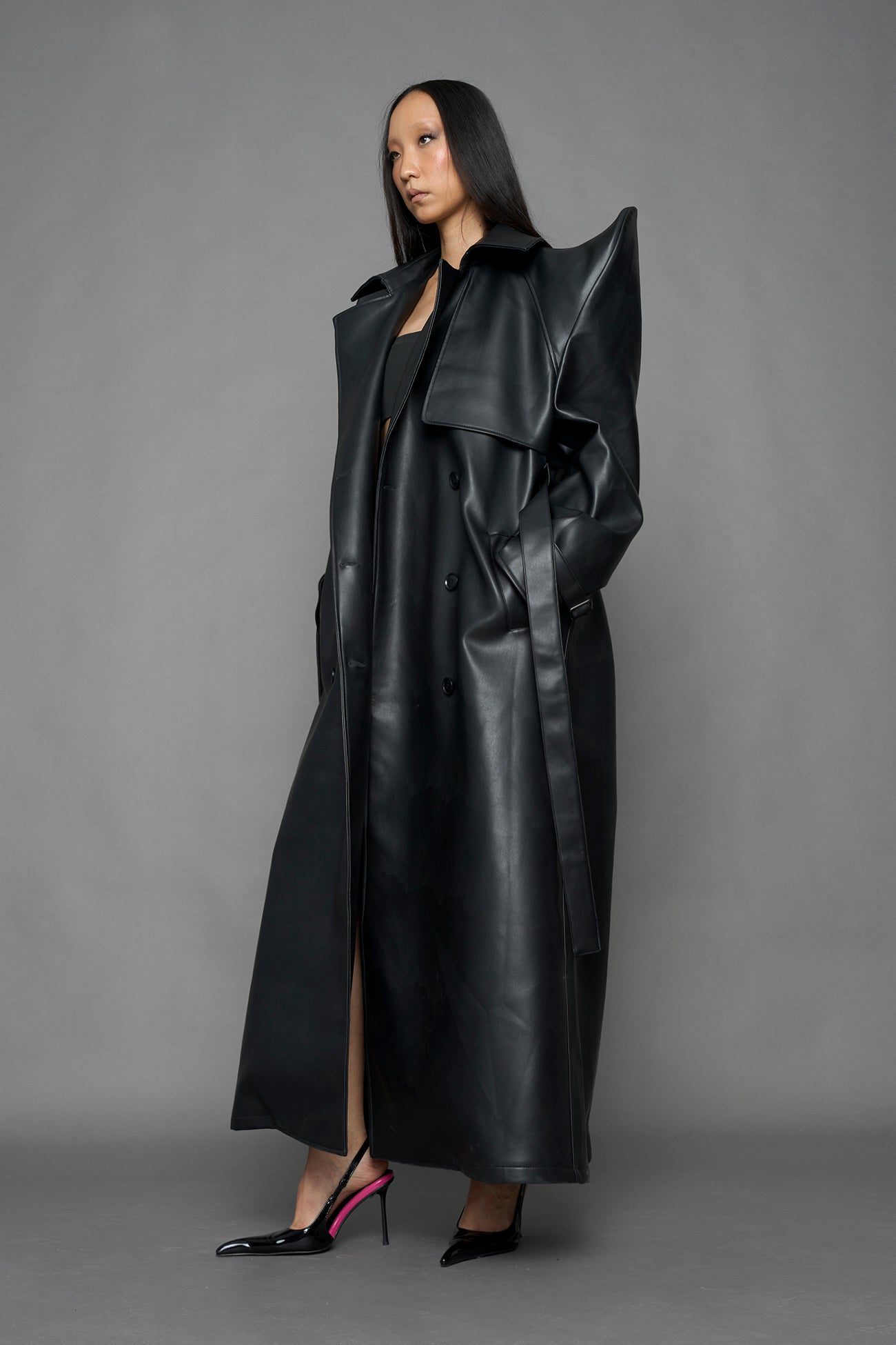 model wearing black vegan leather trench coat with sharp shoulder design